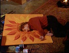 Nick collapses on top of a painting of the sun.